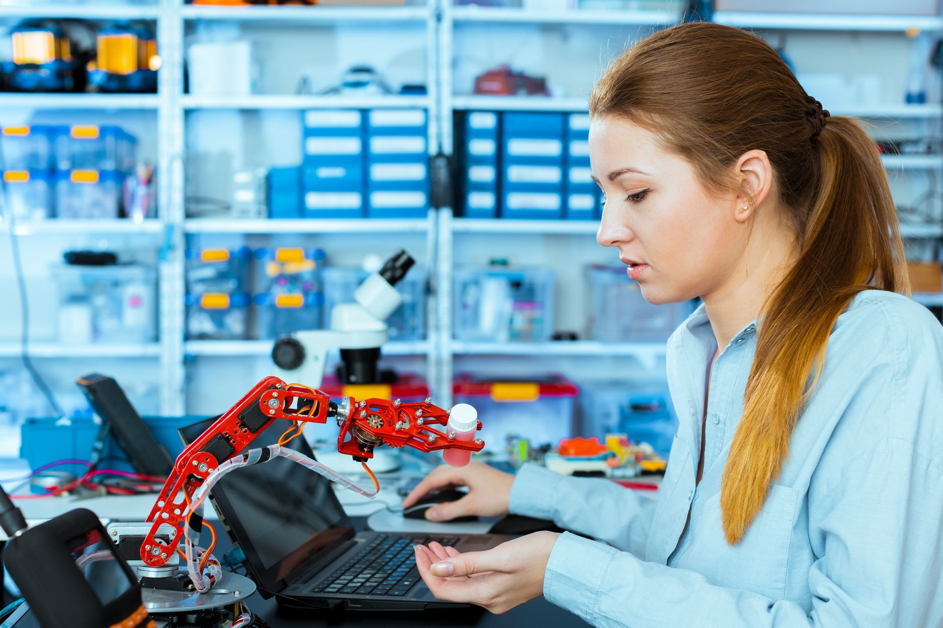 schoolgirl adjusts the robot arm model, girl in a robotics laboratory